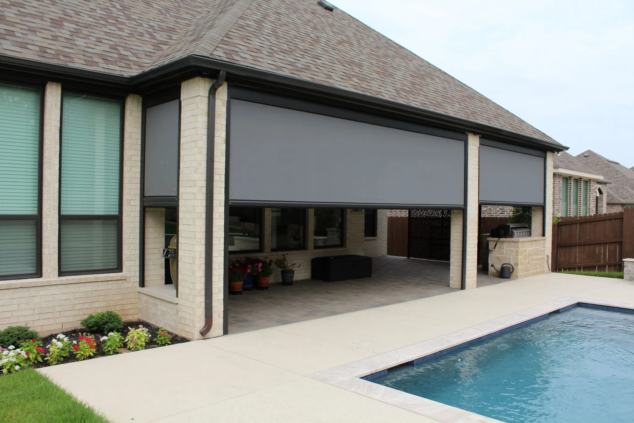 Retractable outdoor sun shade installed on a modern home patio by a swimming pool.