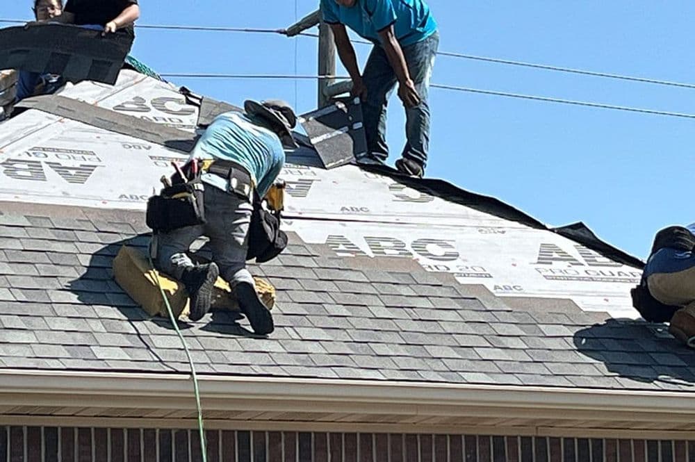 Workers installing roofing materials on a pitch roof under clear blue skies.