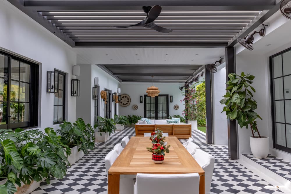 Modern outdoor dining area with checkered flooring and lush greenery, featuring a wooden table.