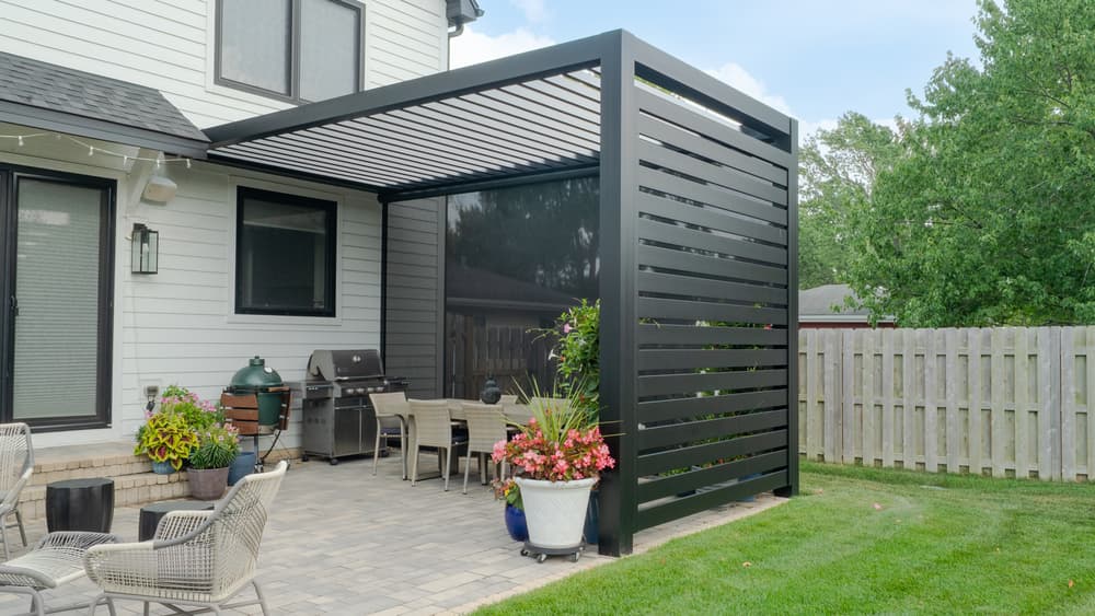 Modern patio with a black pergola, outdoor grill, and vibrant flower arrangements.