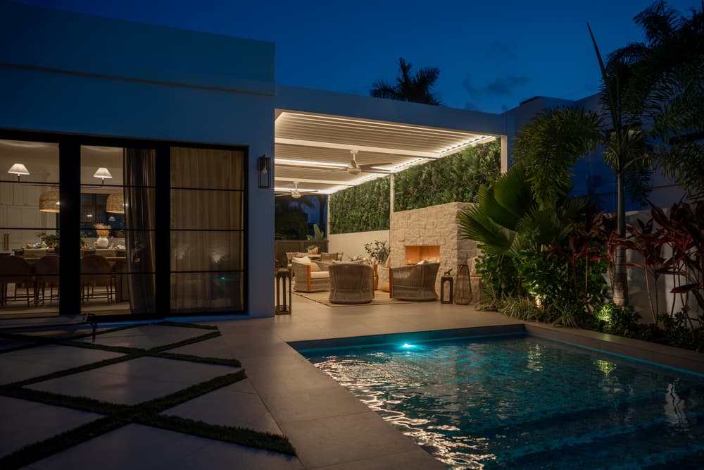 Modern outdoor lounge with pool, illuminated at night, featuring stylish seating and greenery.