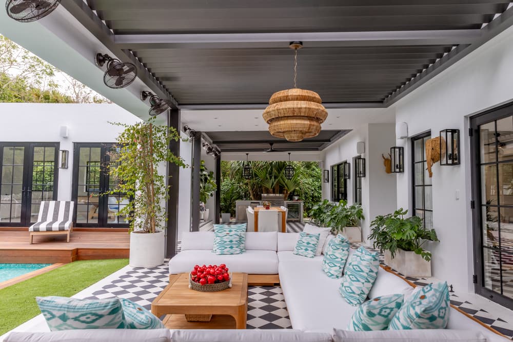 Modern outdoor living space with white seating, decorative cushions, and a pool backdrop.