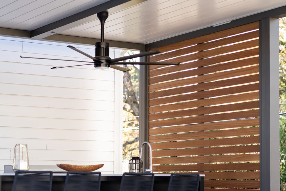 Modern outdoor dining area featuring a black ceiling fan and wooden slatted privacy screen.