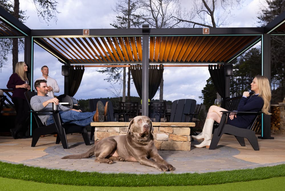 Gathering of friends and family with a dog by a cozy fire pit in an outdoor patio setting.