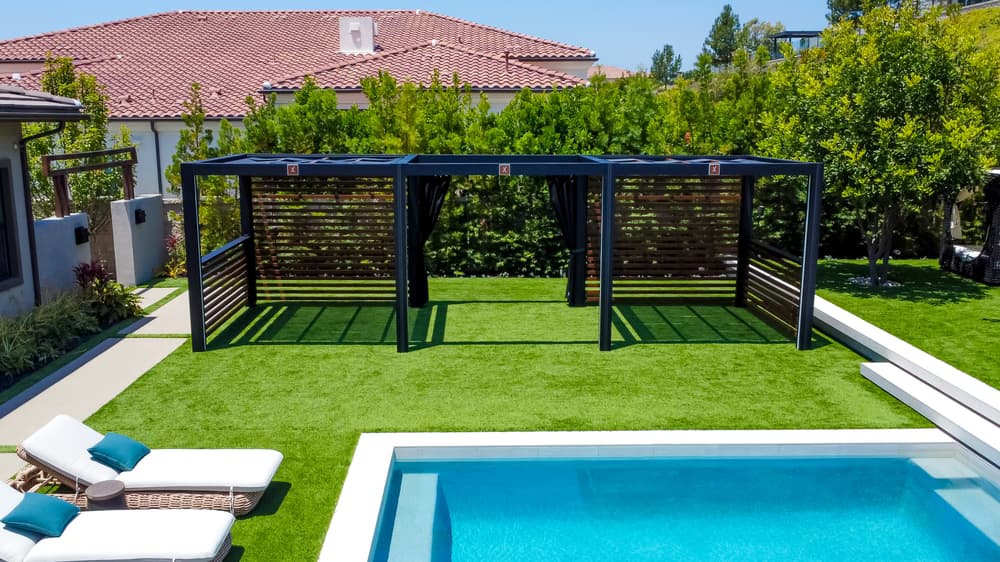 Blue pool with modern pergolas and lounge chairs on a lush green lawn. Sunny backyard oasis.